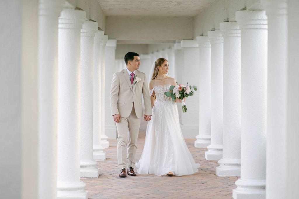Palm Beach bride & groom on their wedding venue posting for phots in a wedding dress with flowers and a formal designer suit.